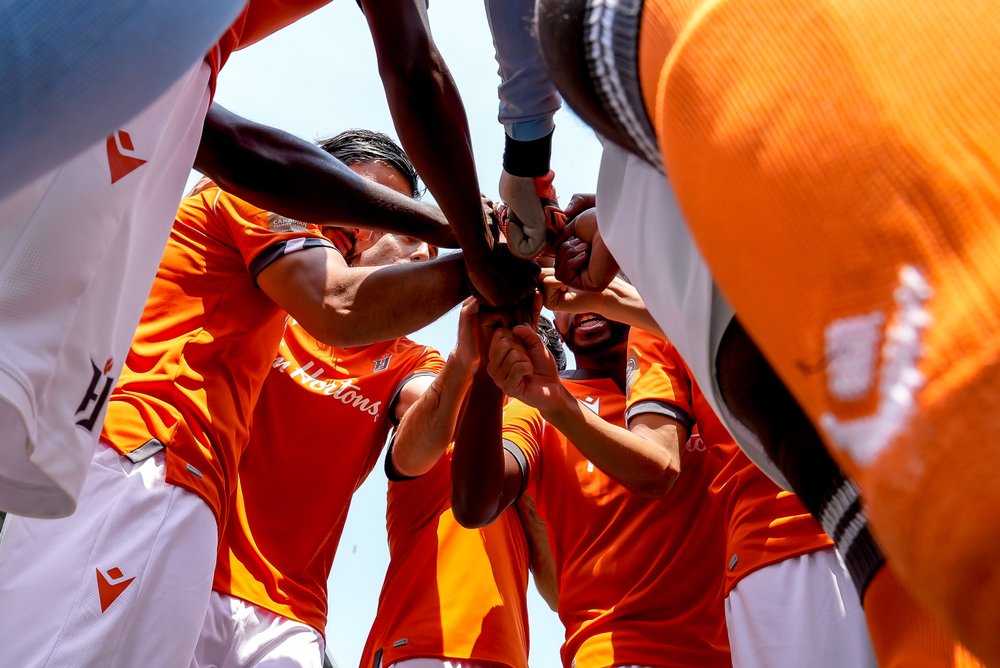 Forge FC players in a huddle with hands in together.