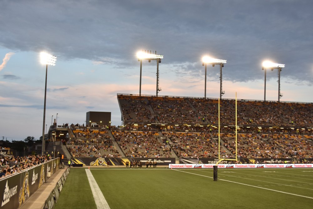 Stands of Tim Hortons Field filled with fans at dusk.
