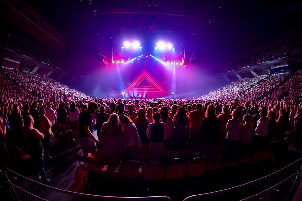 Full crowd on the floor at a concert with lights on stage.