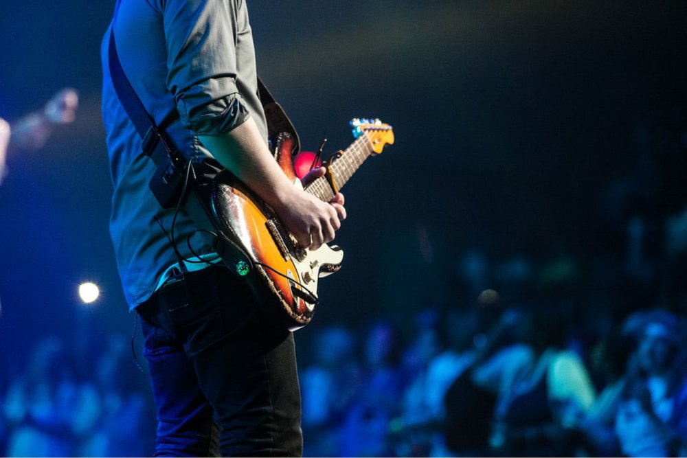 Guitar player on stage performing at a concert for full crowd.