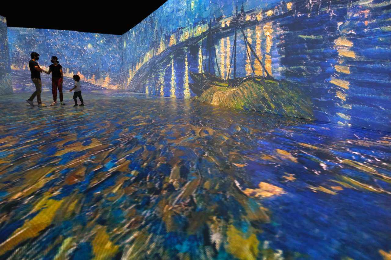 Man, woman and child standing in middle of 3D image of Van Gogh painting projected on floor and wall around them.