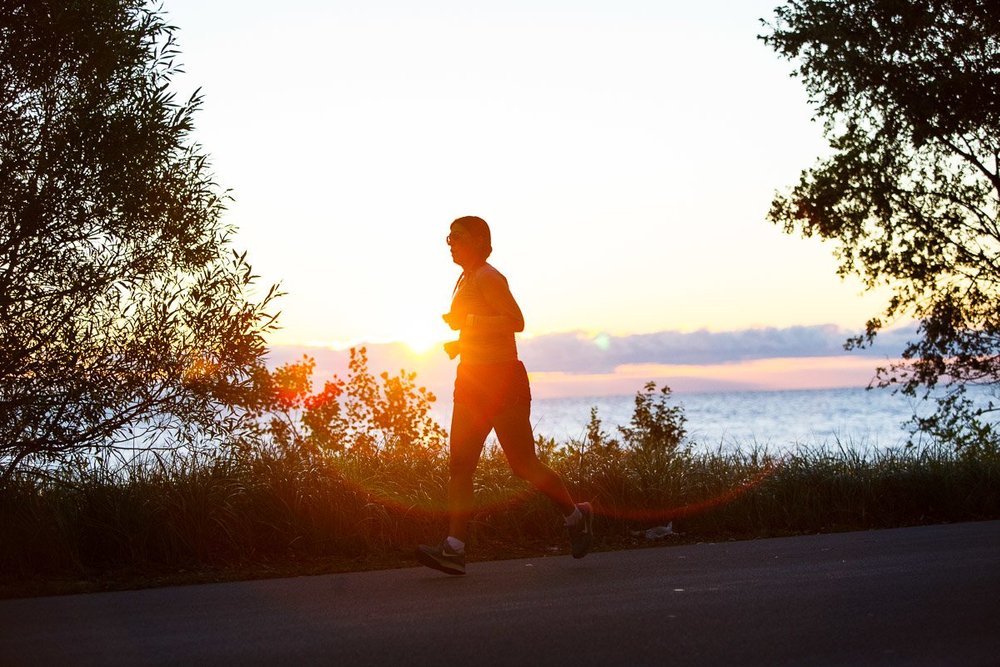Woman running along Confederation Park beachfront trail at sunset.