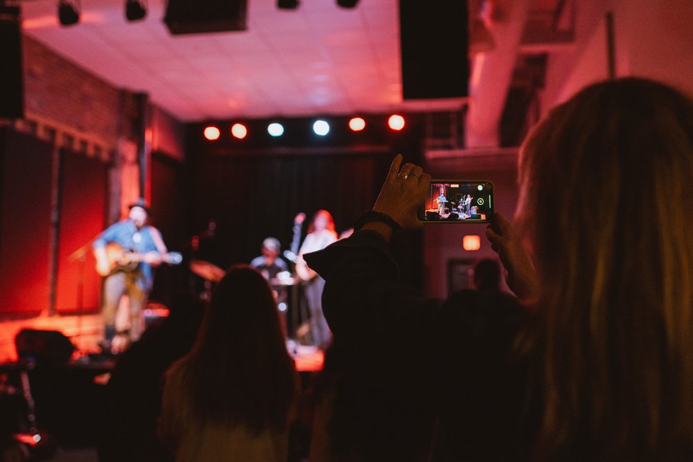 Person in audience taking a photo of band performing on stage.