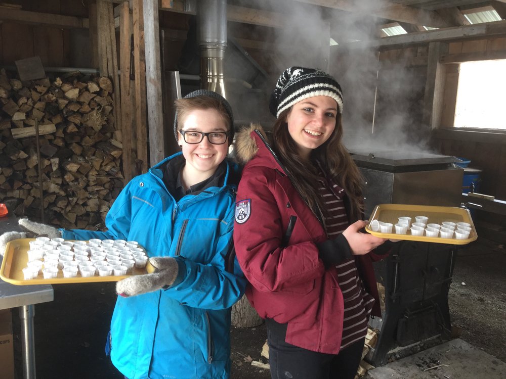 Two young people smiling and holding trays of maple syrup cups.