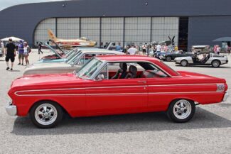 Vintage cars with military arcrafts in the background at Canadian Warplane Heritage Museum.