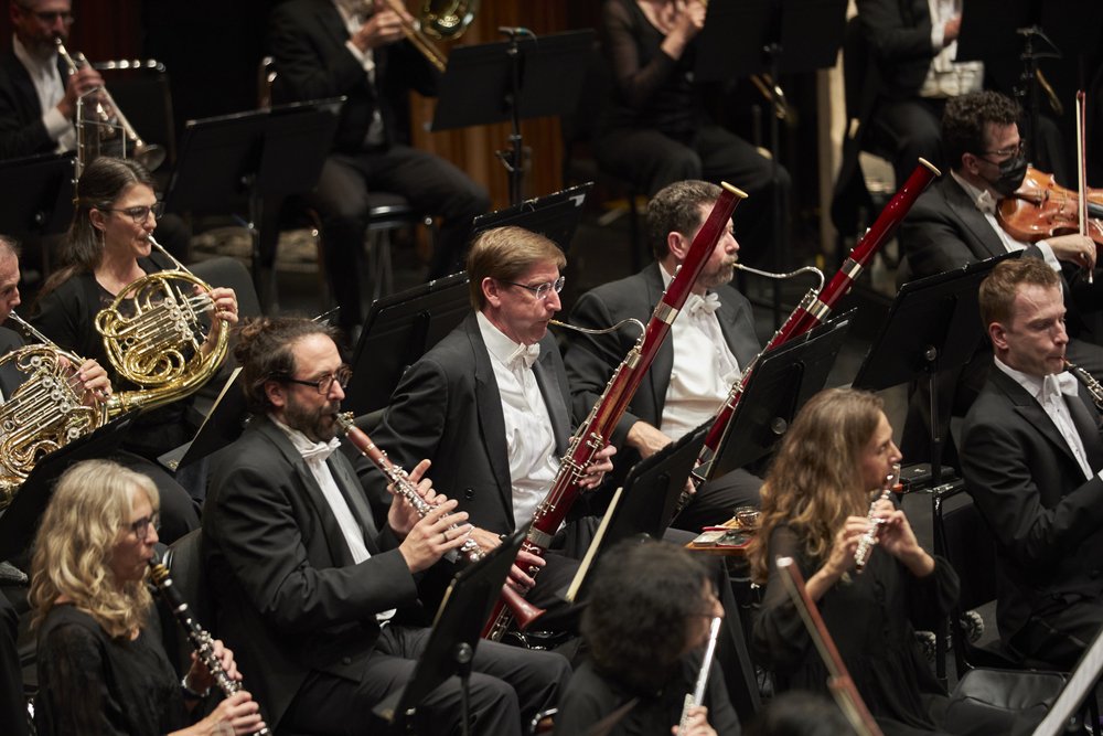 Conductor standing in front of orchestra on stage.