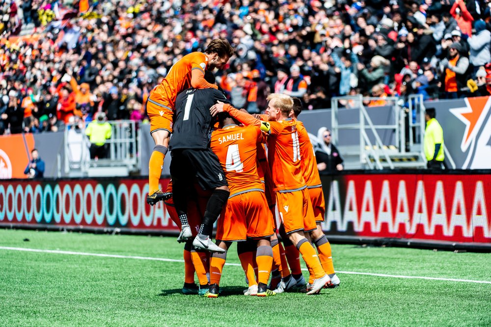 Forge FC players jumping together on field celebrating a goal.