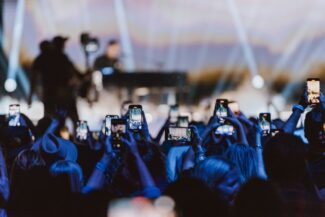 Concert audience cheering at stage and holding up phones.