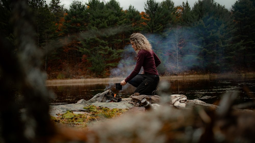 Woman starting campfire with ake and mountain views behind her.