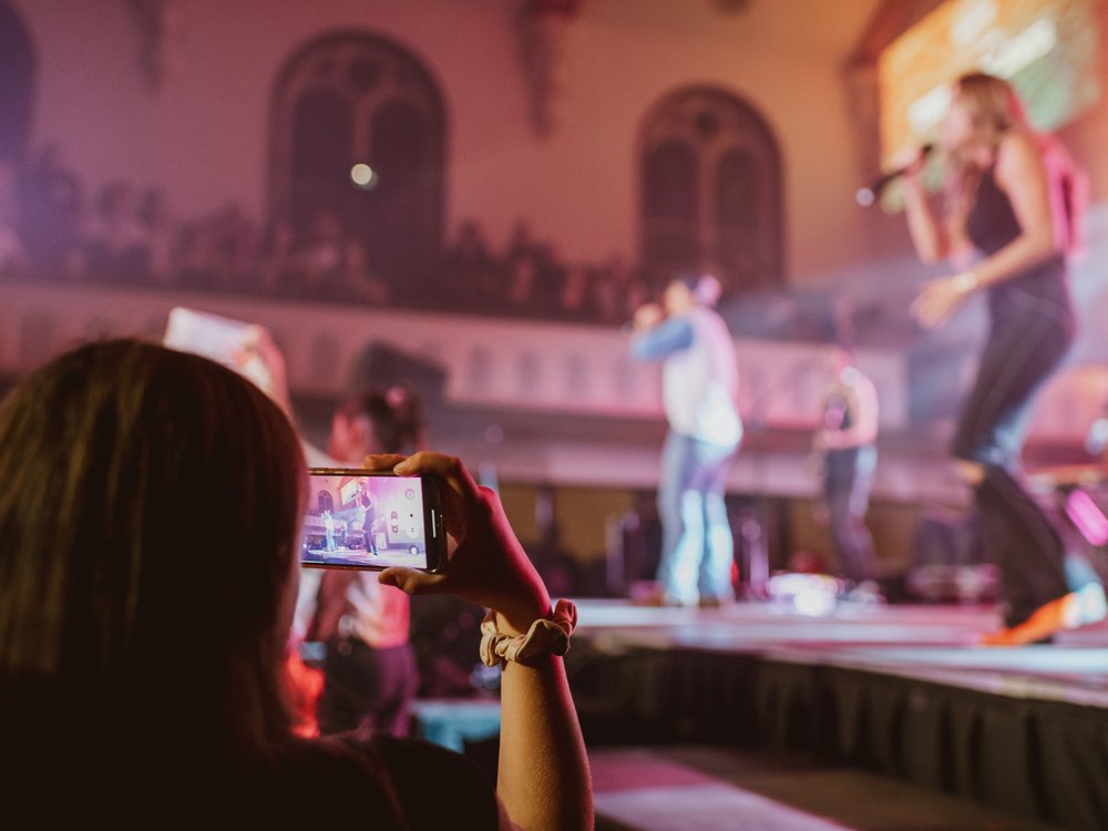 Fan in front row takin picture of two performers on stage at The Music Hall.