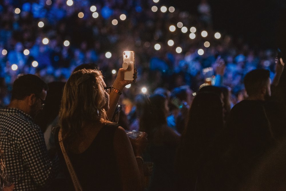 Person standing in full crowd taking a photo of the stage at an event.