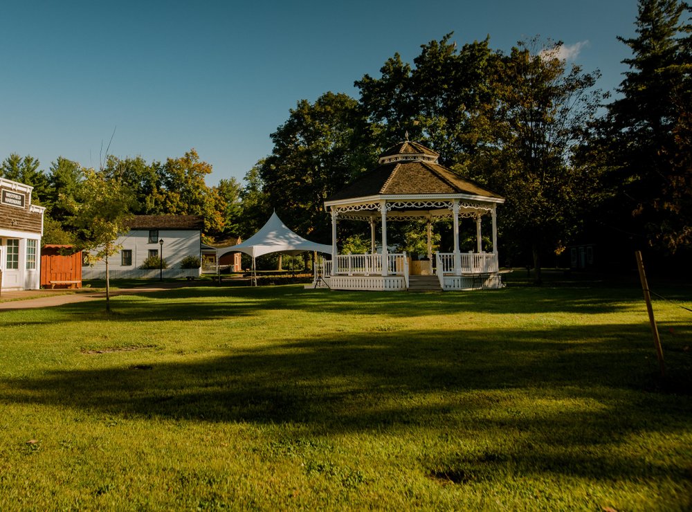 White gazebo in the middle of Westfield Heritage Village surrounded by green trees in summer.