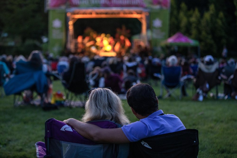 Couple sitting in the garden at RBG watching a performance on stage.