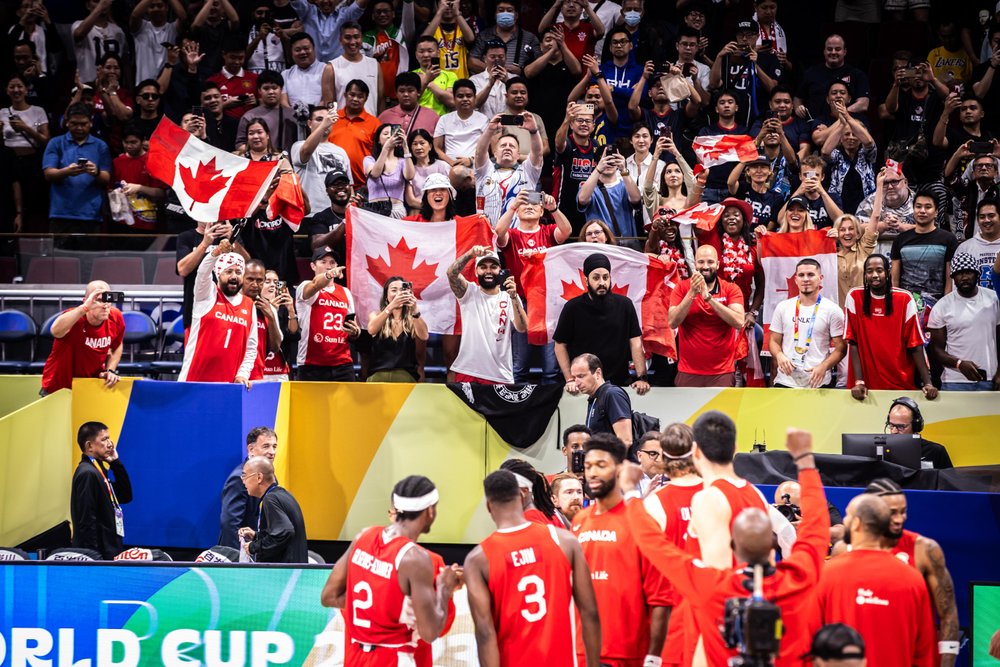 Team Canada basketball team celebrating on court with fans cheering them on.
