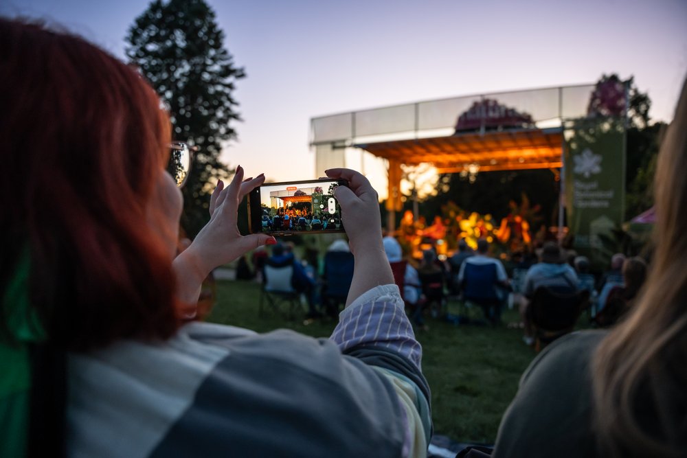 Woman taking photo of outdoor concert in Hendrie Park.