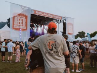 Attendees standing near the main stage at the Because Beer Craft Beer Festival in Hamilton, with a couple in the foreground and stage lights glowing in the background.