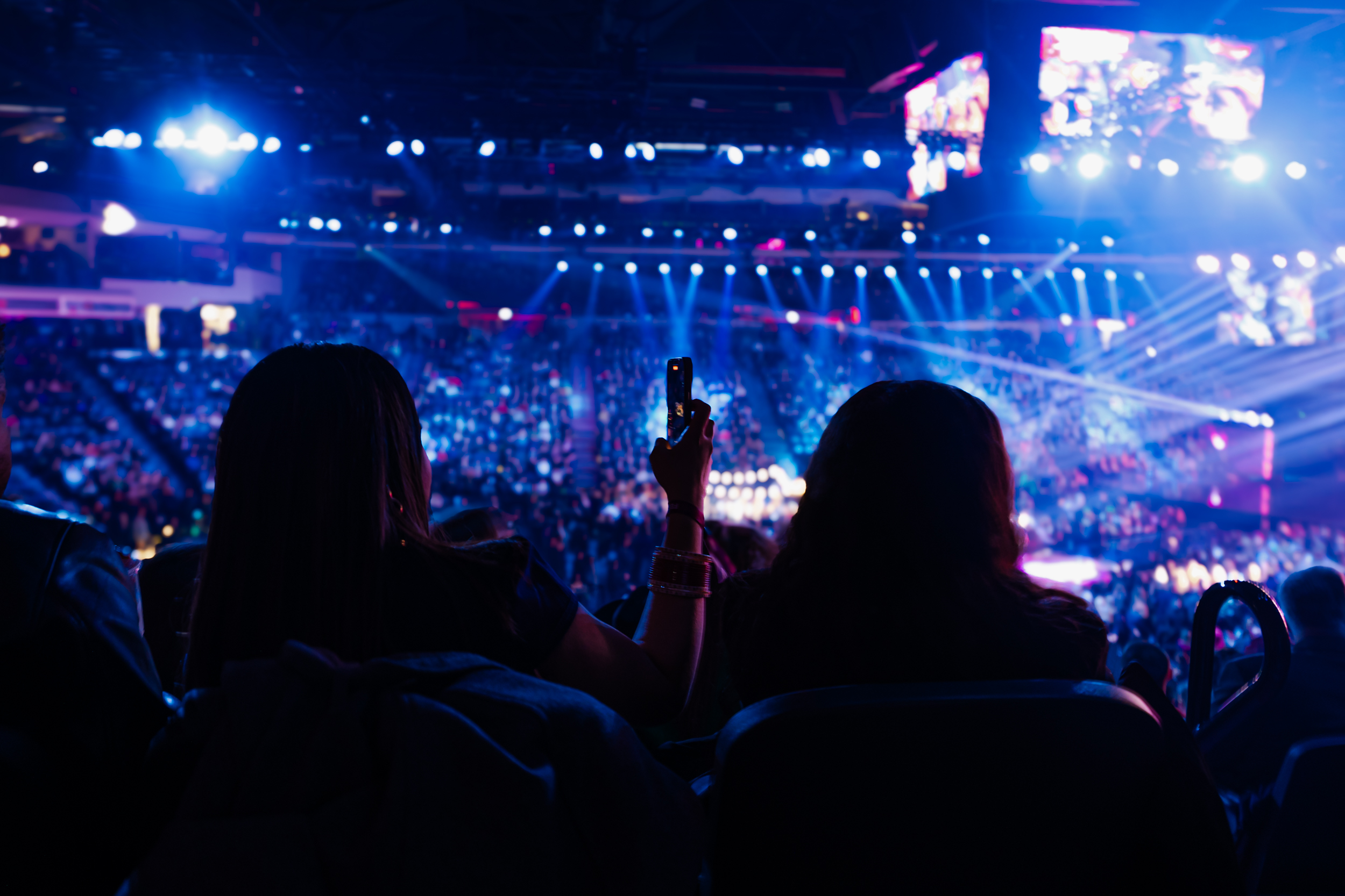 Two people sitting in the crowd taking a video of the stage.