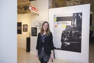 Curator Meredith Leonard smiling in the Punching In exhibition, beside a large panel asking 