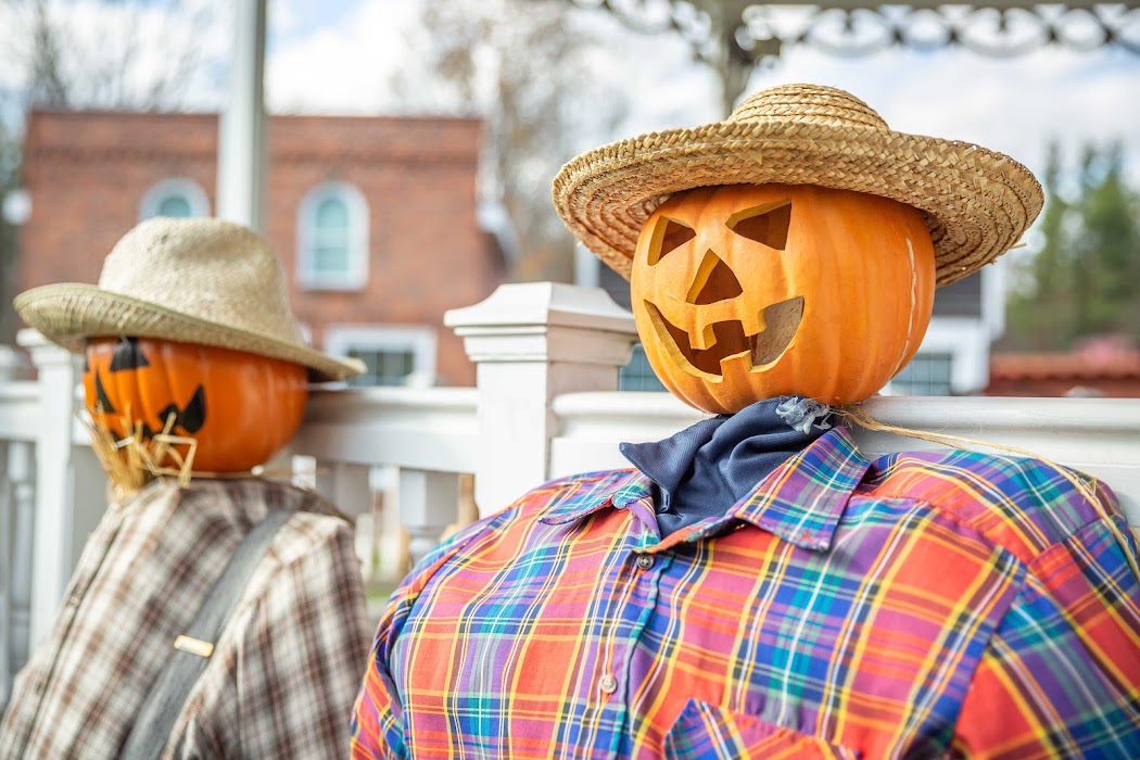 Two jack-o-lanterns sit on top of straw people.