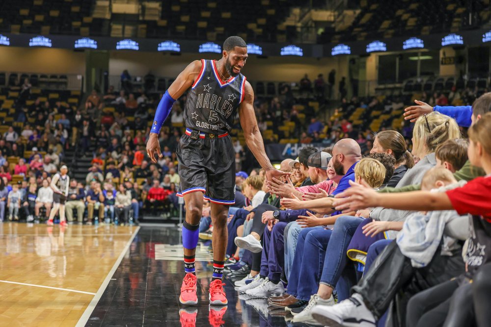 Harlem Globetrotter player on court high-fiving fans in the front row.