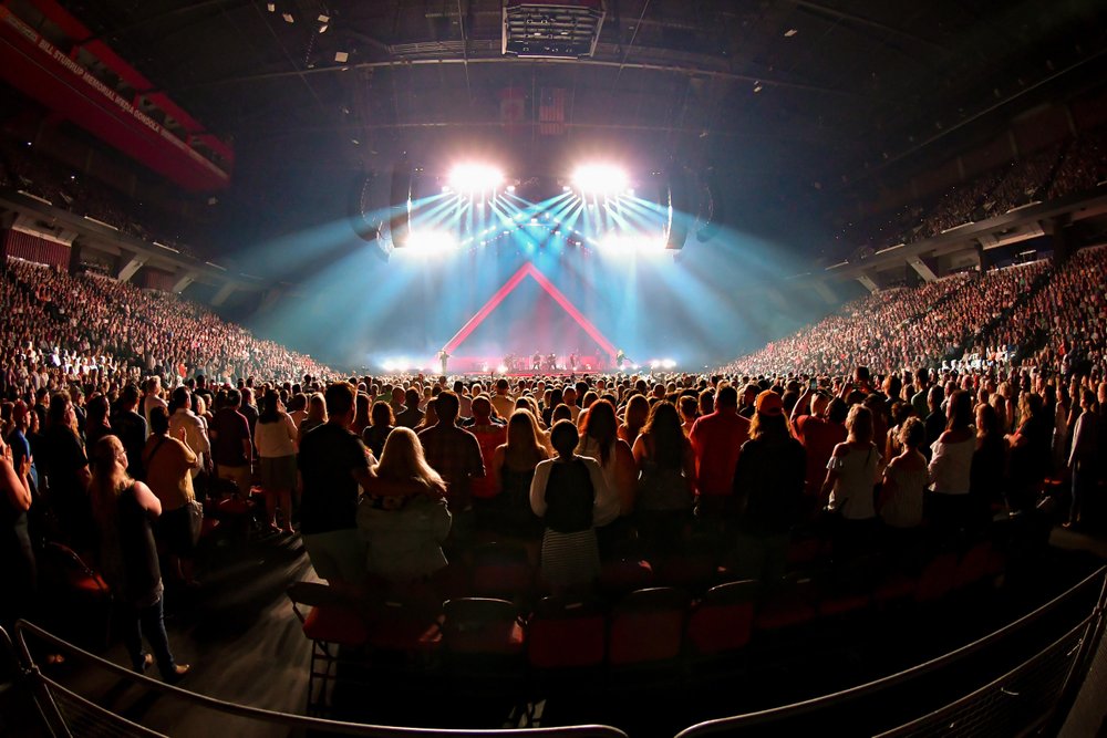 Full lights on stage with crowd in the floor at a concert.