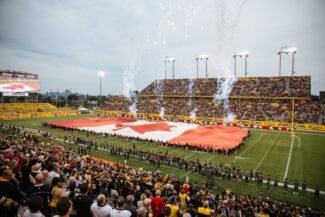 Canadian flag on the field with fireworks at the start of the game.